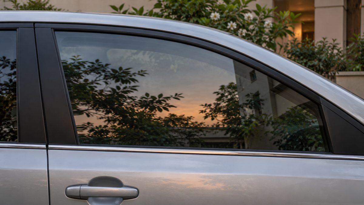 The side of a silver car stands beside greenery in a quiet apartment courtyard in early evening light.