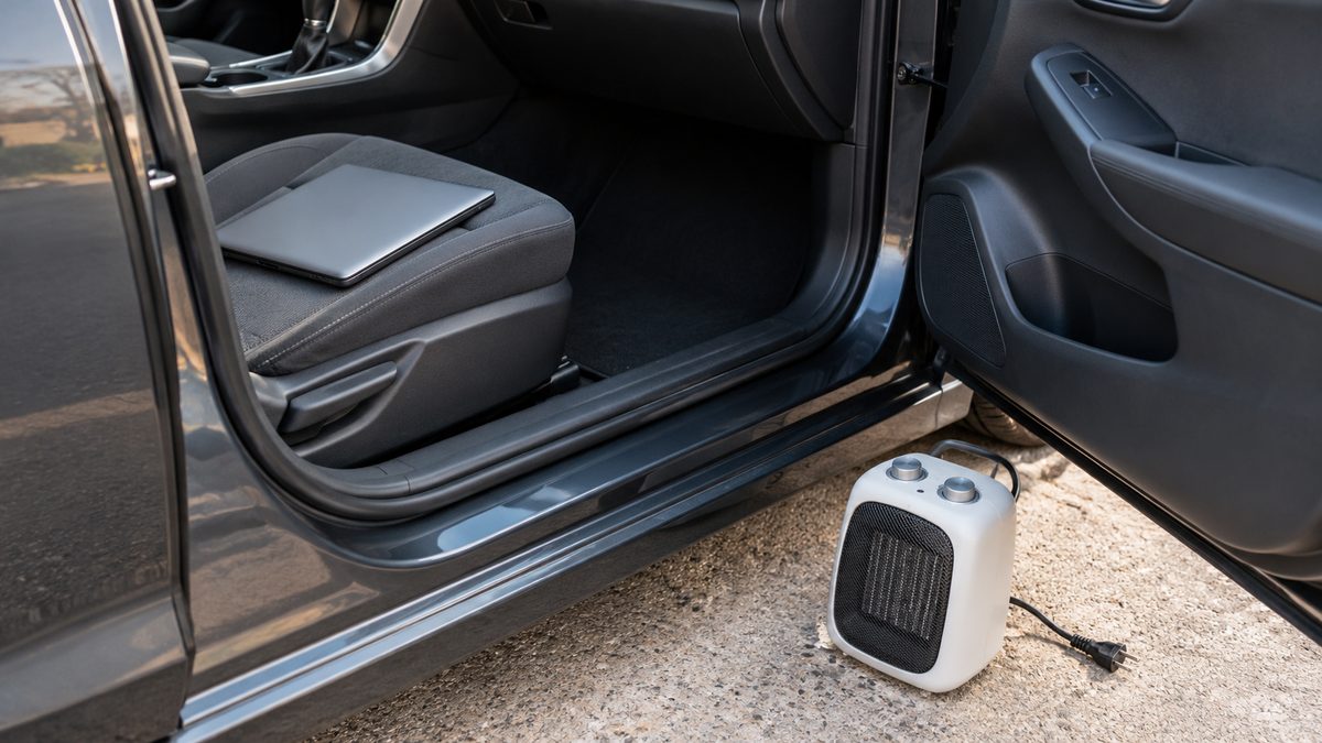 An unplugged compact heater sits outside an open car door, with a closed laptop on the passenger seat.