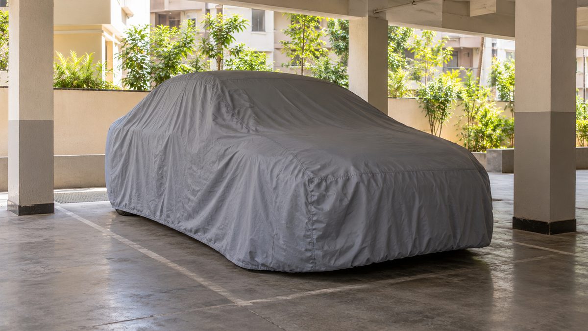 A car under a plain grey cover stands between unmarked pillars in a quiet apartment parking space.