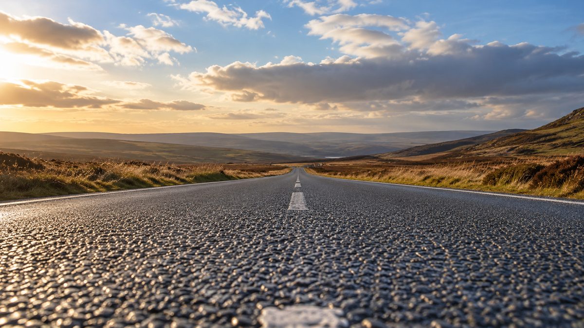 An empty moorland road runs toward the horizon beneath an expansive, softly clouded sky.