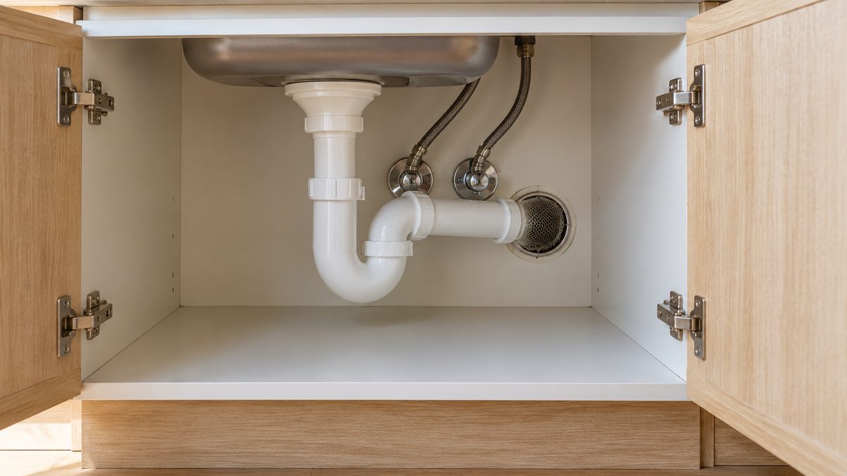 Metal mesh fills a pipe opening inside a tidy under-sink cupboard with its doors open.